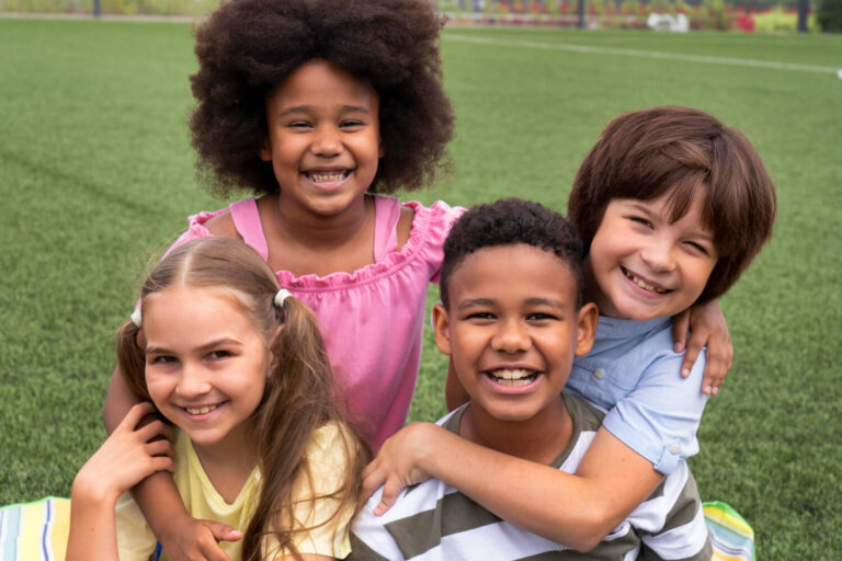 Grupo de crianças diversas sorrindo em um gramado, ilustrando os benefícios do Invisalign First para crianças na Mooca.