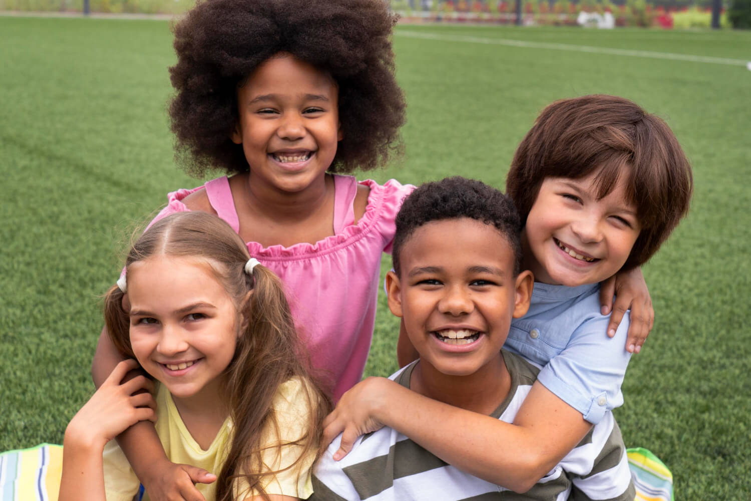 Grupo de crianças diversas sorrindo em um gramado, ilustrando os benefícios do Invisalign First para crianças na Mooca.
