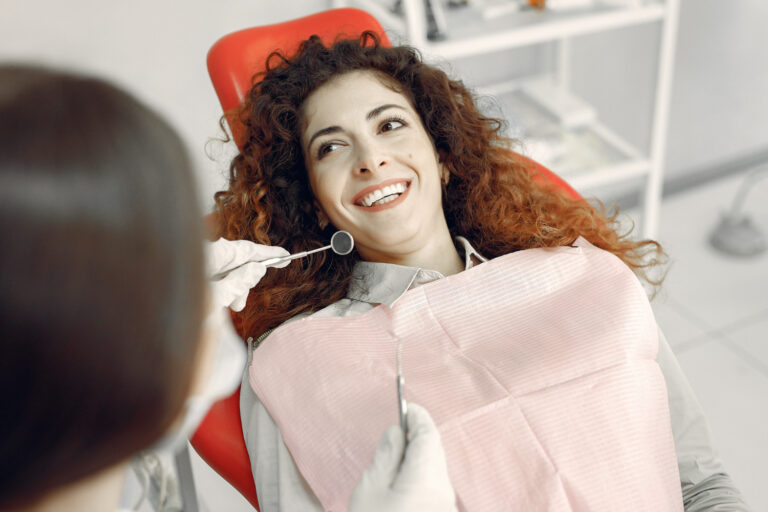 Paciente sorrindo na cadeira da Clínica AGN Odontologia após clareamento dental na Mooca, SP, enquanto dentista segura espelho clínico.