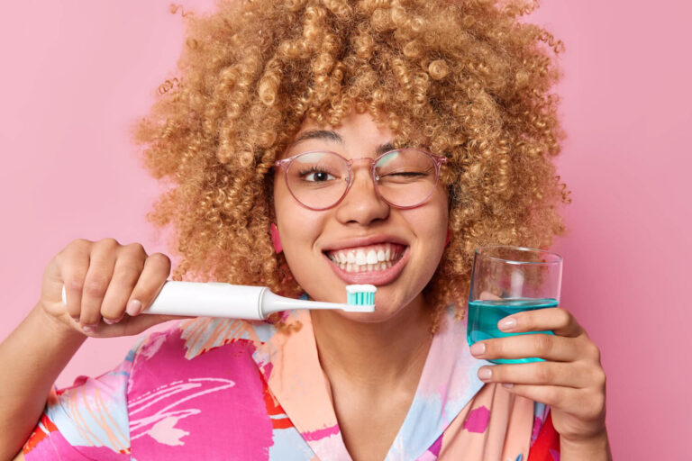 Mulher sorridente segurando escova elétrica e enxaguante bucal, exemplificando a higiene facilitada pelo ClearCorrect na Mooca.