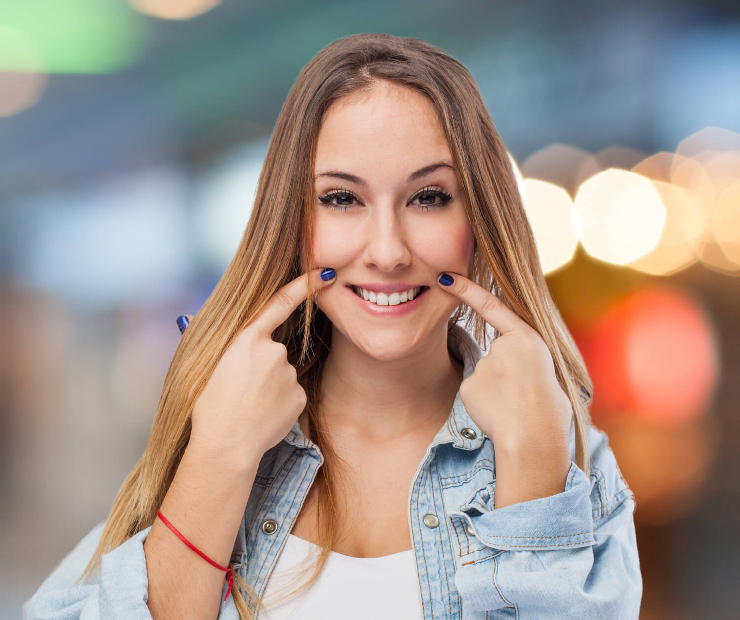 Mulher jovem sorri e aponta para os dentes, ilustrando o resultado de facetas de resina e porcelana na AGN Odontologia, Parque da Mooca.