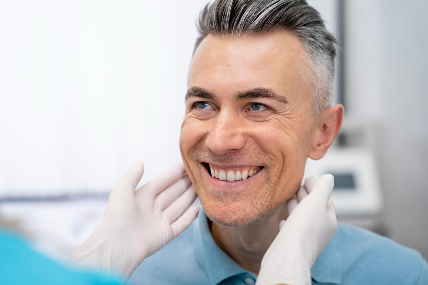 Homem de cabelo grisalho sorrindo enquanto dentista avalia sua estrutura facial para implante dentário na Mooca na AGN Odontologia.