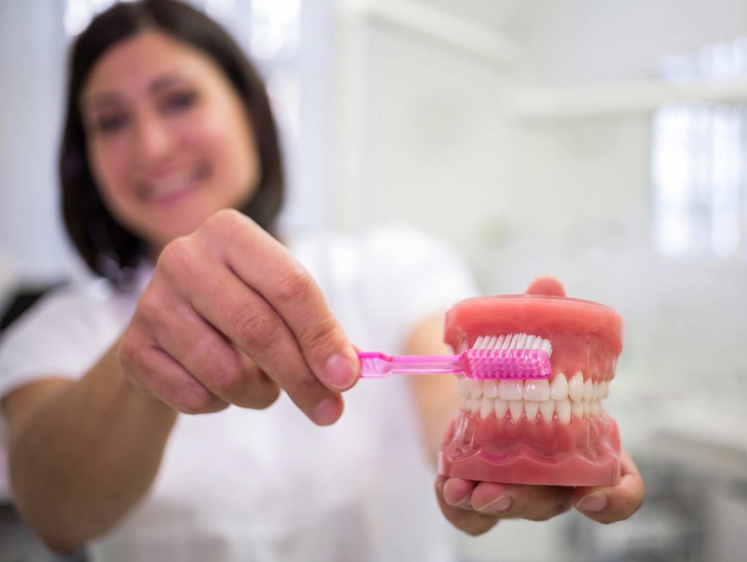 Dentista demonstrando como limpar prótese protocolo com escova rosa em modelo bucal na AGN Odontologia, na Mooca.