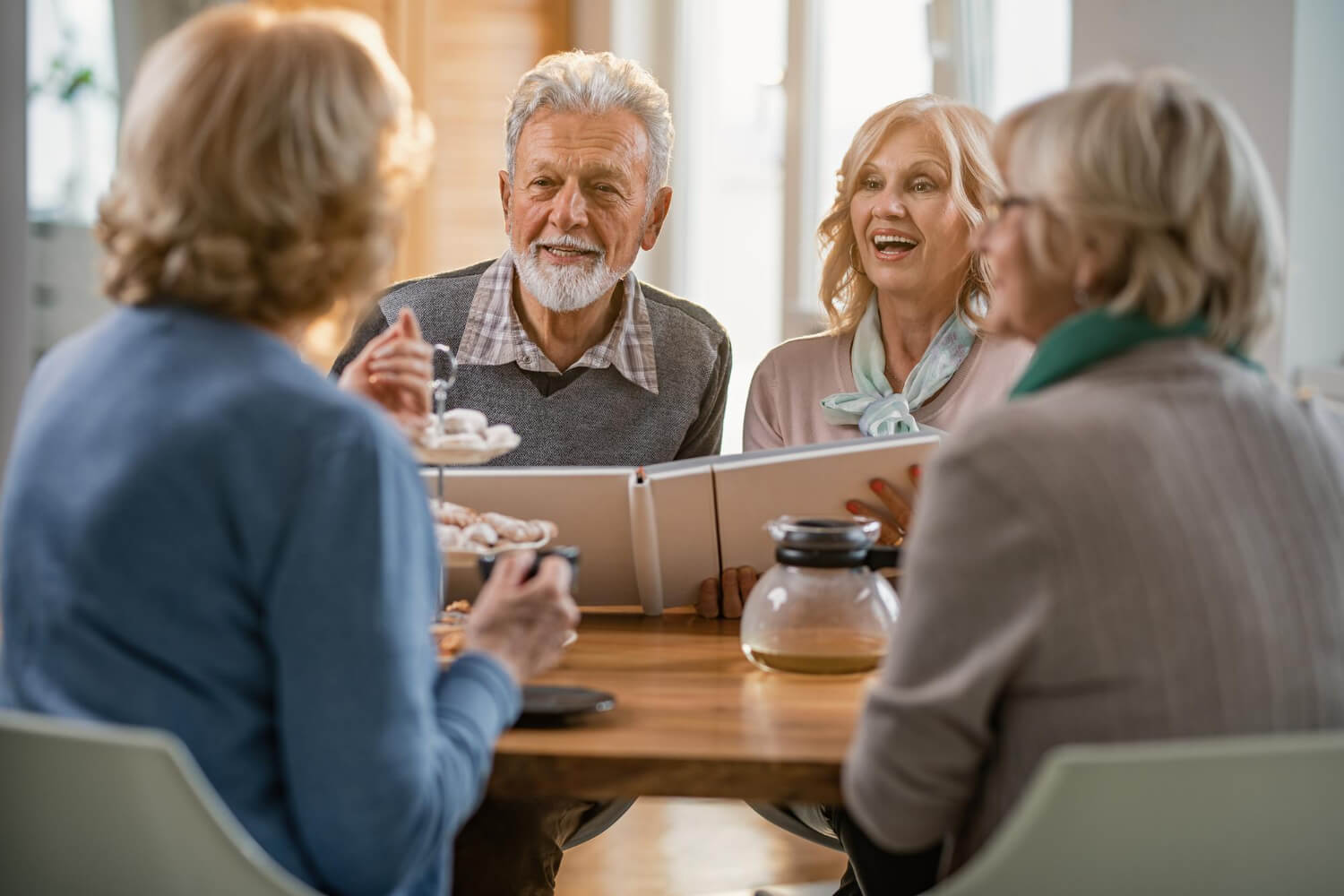 Grupo de idosos sorrindo reunidos em uma mesa, mostrando a liberdade ao conversar com sua prótese protocolo na Mooca na AGN Odontologia.