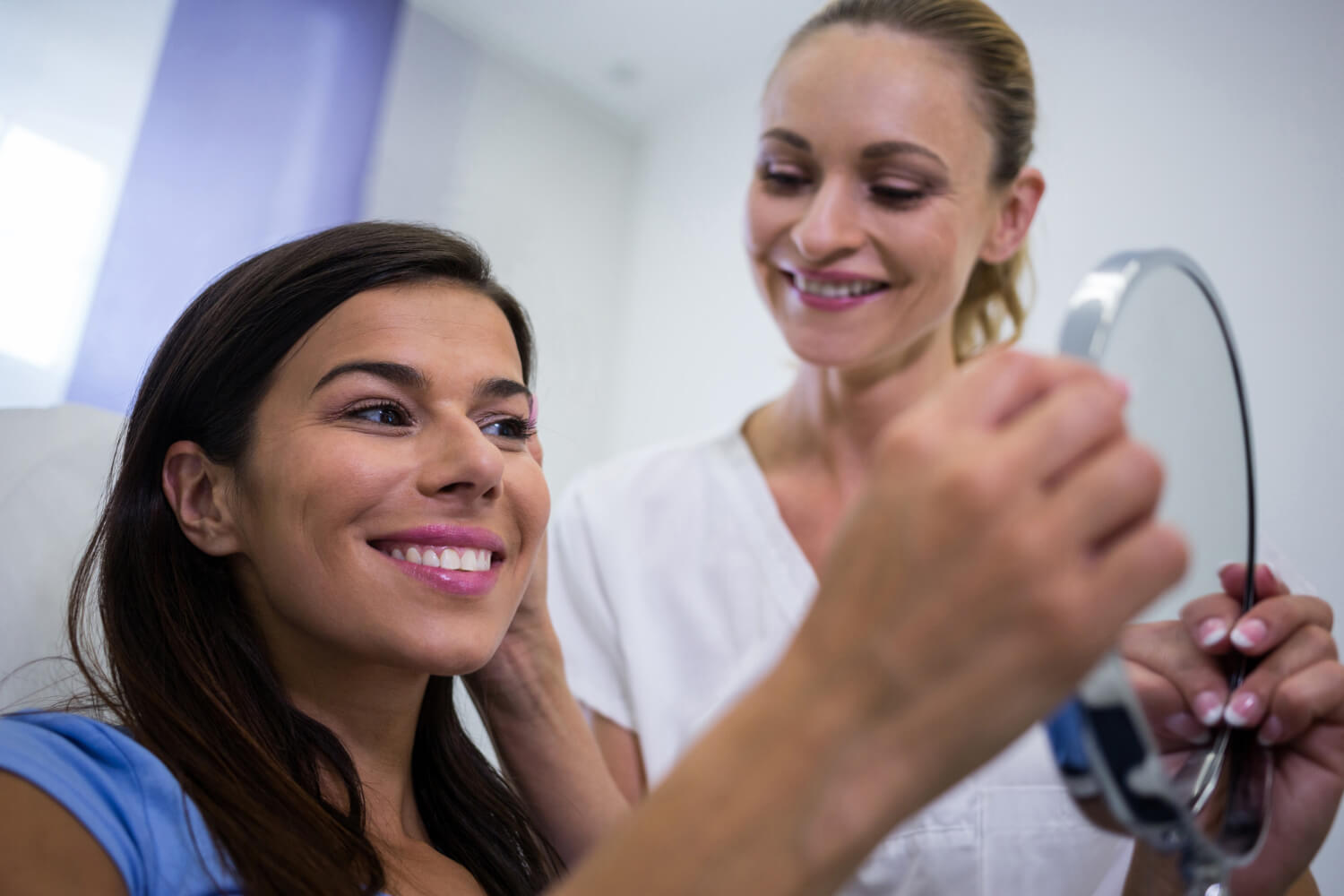 Paciente sorrindo ao ver seus dentes novos no espelho. Tratamento de implante dentário com dente fixo na AGN Odontologia na Mooca.