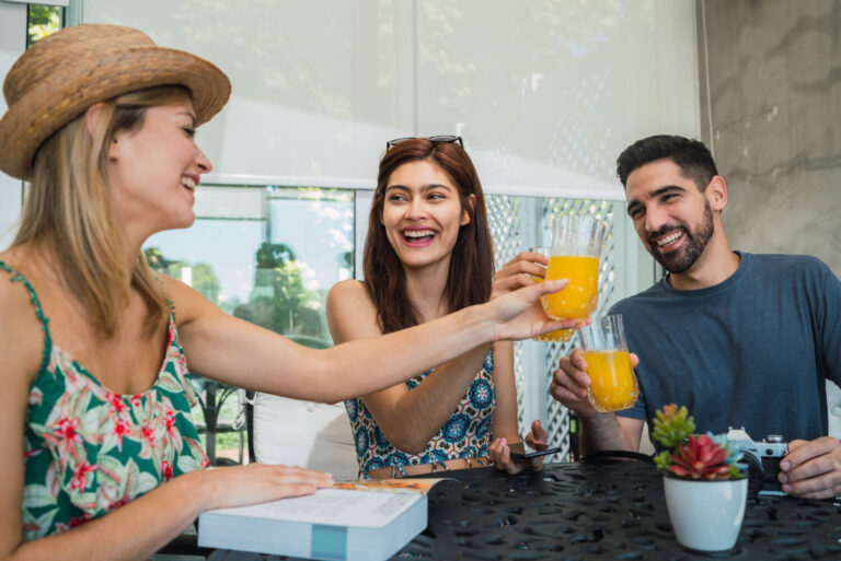 Três jovens amigos sorrindo e brindando com copos de suco de laranja em um café na Mooca, ilustrando o uso de alinhadores invisíveis.