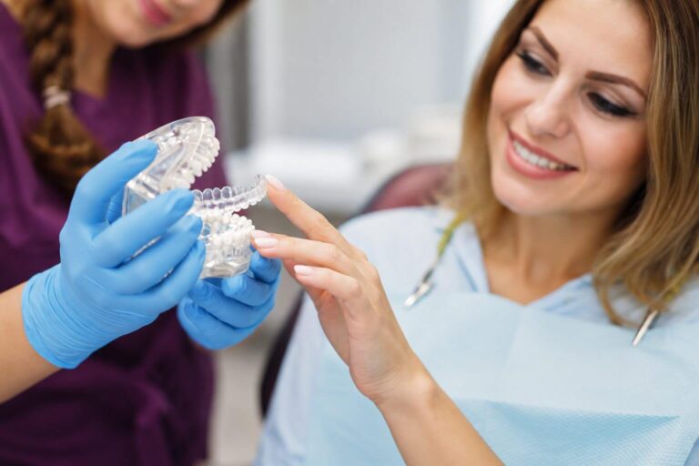 Paciente sorrindo enquanto dentista demonstra o uso de alinhadores invisíveis em modelo dentário na clínica AGN Odontologia na Mooca.